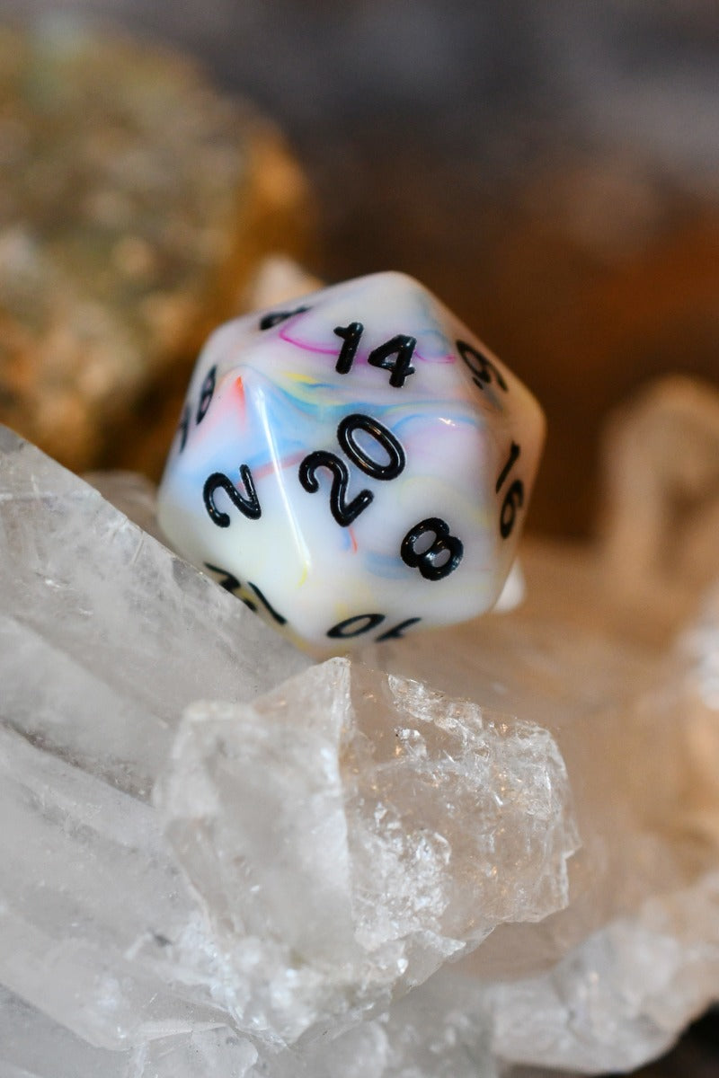 A marbled white 20-sided die with pastel swirls of pink, blue, and yellow, featuring black printed numbers, resting on clear quartz crystals.