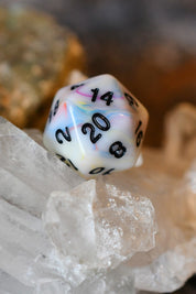 A marbled white 20-sided die with pastel swirls of pink, blue, and yellow, featuring black printed numbers, resting on clear quartz crystals.