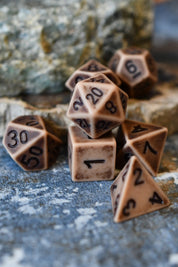 A set of brown polyhedral tabletop gaming dice with black printed numbers, arranged on a textured stone surface with a blurred natural rock background.