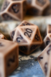 A close-up of tan polyhedral gaming dice with dark engraved numbers, including a 20-sided die in sharp focus and other dice blurred in the background.