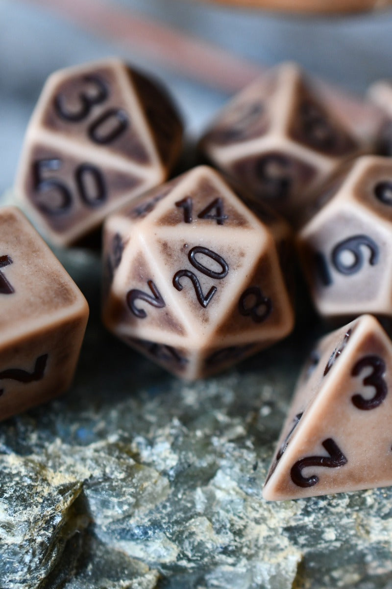 A set of brown polyhedral tabletop gaming dice with dark engraved numbers, arranged on a textured stone surface.