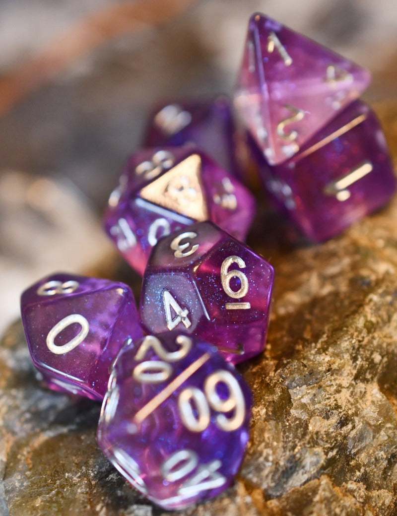 A set of translucent purple polyhedral gaming dice with white numbers, arranged on a textured brown rock surface.