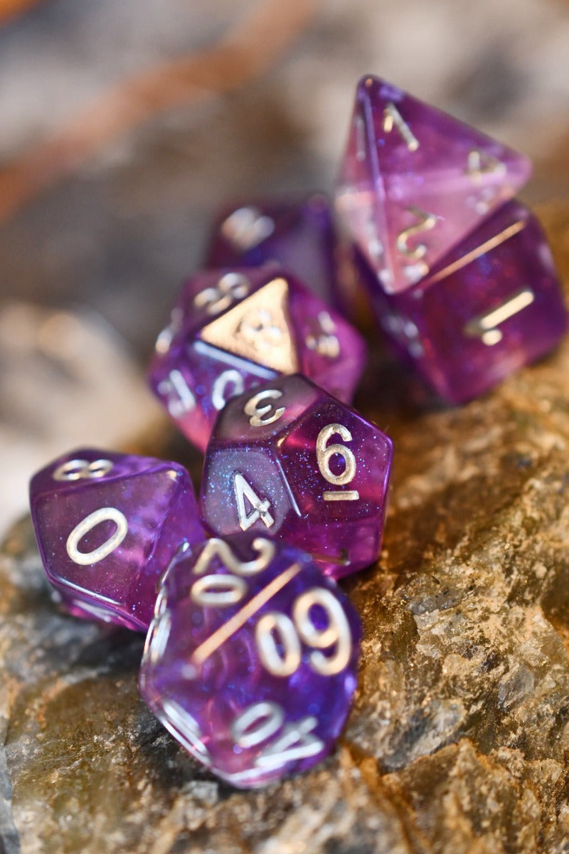A set of translucent purple polyhedral gaming dice with white numbers, arranged on a textured brown rock surface.