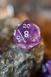 A translucent purple polyhedral die, showing an 8 with white numbering, resting on a textured rock with a blurred background.