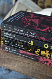 A stack of four horror book spines resting on a wooden surface. The books are titled 'All the Fear of the Fair', 'Possessed', 'Out of the Past', and 'Dead Drunk', with black covers featuring red and gold illustrations.