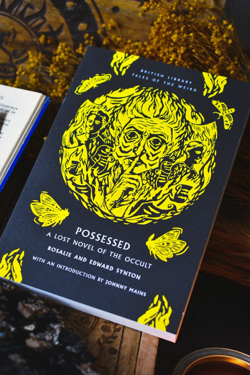 The book 'Possessed: A Lost Novel of the Occult' by Rosalie and Edward Synton, featuring a dark navy blue cover with a large yellow illustration of a possessed face and butterflies, styled on a rustic wooden surface.