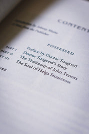 A close-up, angled view of a book's table of contents page, showing the title 'POSSESSED' and chapter titles printed in black on off-white paper.