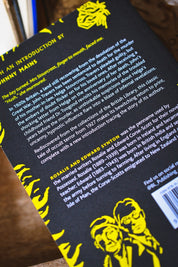 Close-up of the back cover of a book titled POSSESSED featuring a black background with yellow illustrated flames and white text, photographed on a wooden surface.